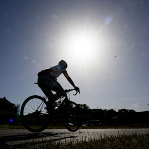 Ein Rennradfahrer fährt am Morgen auf dem Elberadweg am Blockhaus entlang, während am Himmel die Sonne scheint.