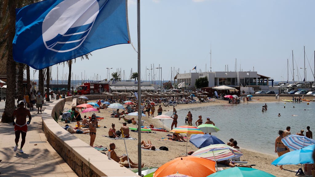 Eine blaue Flagge weht am Strand der Bucht Cala Estancia im Wind.