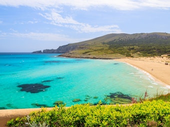 Der Strand in der Cala Mesquida auf Mallorca mit seinen weiten Dünen, dem türkisfarbenem Wasser und dem saftigen Grün der Pflanzen.