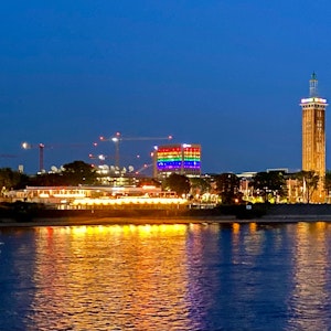 Ein Blick auf Köln-Deutz in der Dunkelheit. Ein Gebäude zeigt sich in Regenbogenfarben.