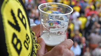 Ein Dortmunder Fan hält im Stadion einen Bierbecher in der Hand.