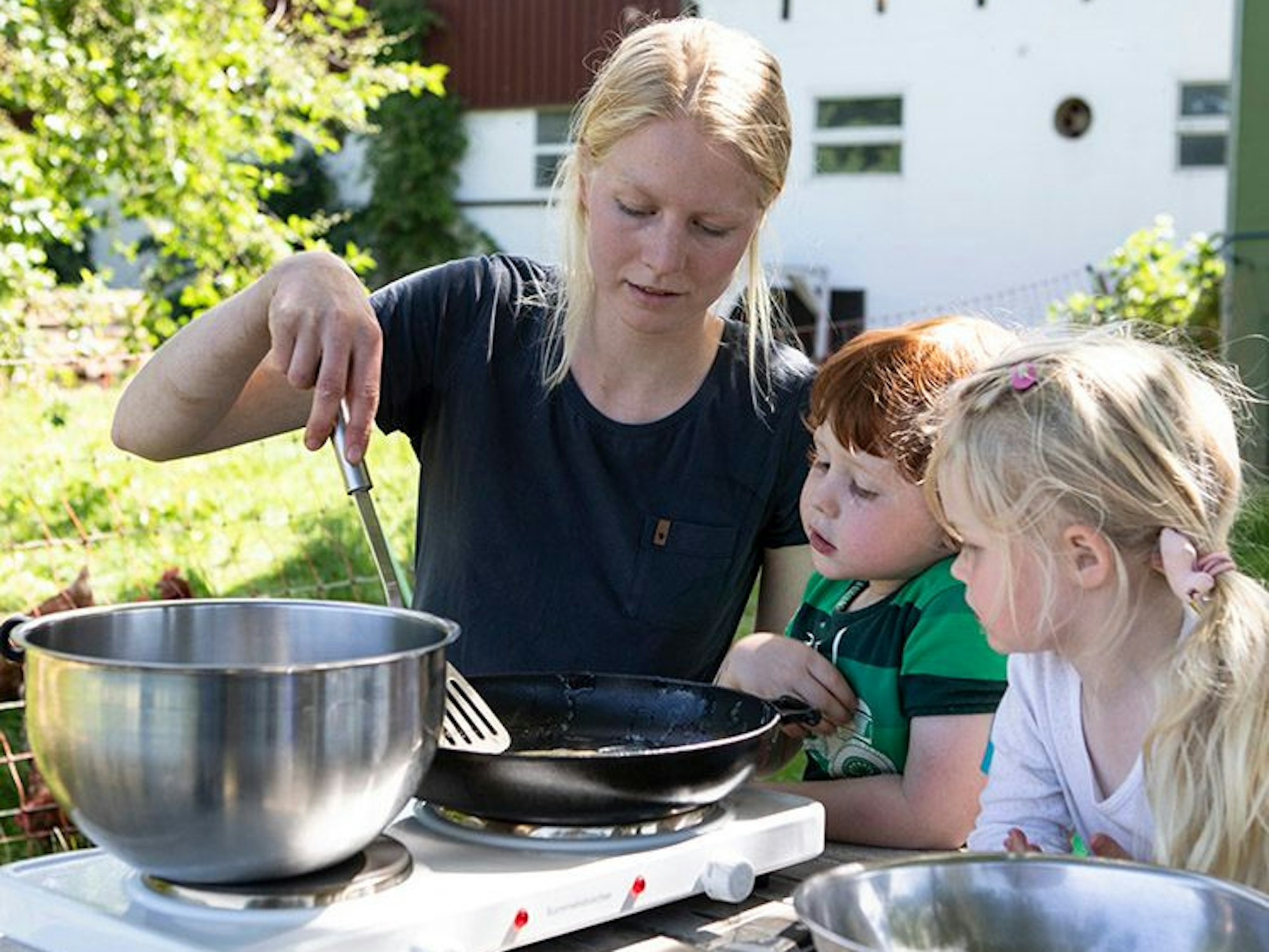 Zwei Kinder bereiten mit Landwirtin Carolin Lawnik Kräuterpfannkuchen zu.