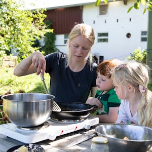 Zwei Kinder bereiten mit Landwirtin Carolin Lawnik Kräuterpfannkuchen zu.