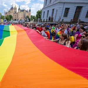 Mit einer großen Regenbogenfahne ziehen Teilnehmerinnen und Teilnehmer einer CSD-Parade in Berlin mit.