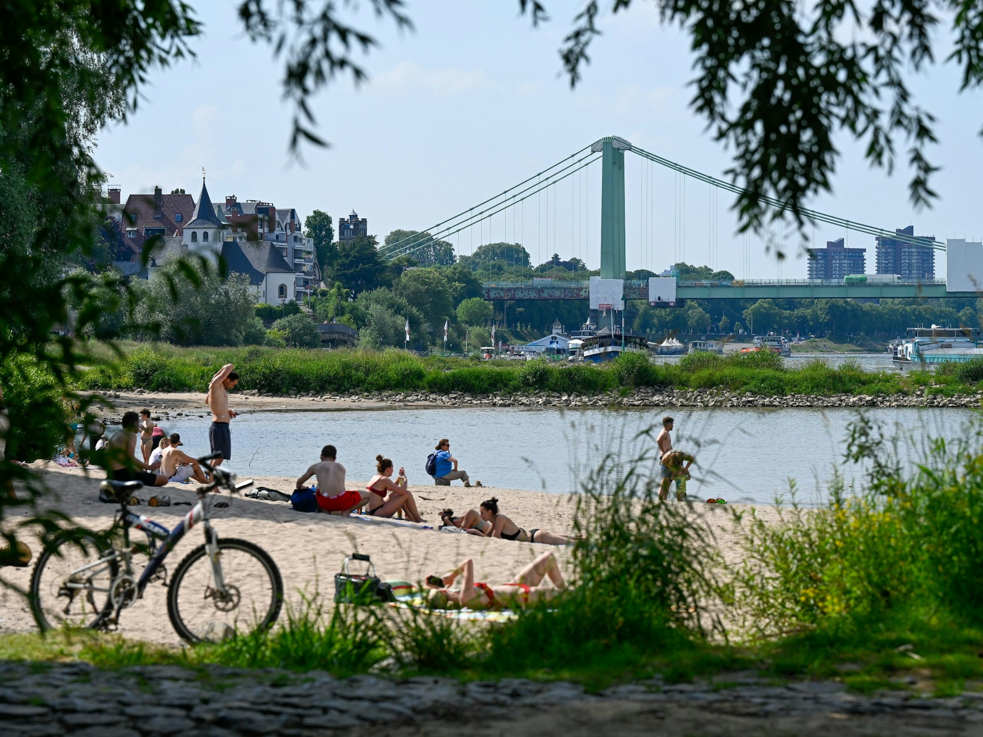 Menschen liegen in Badekleidung am Strand am Rodenkirchener Rheinufer.
