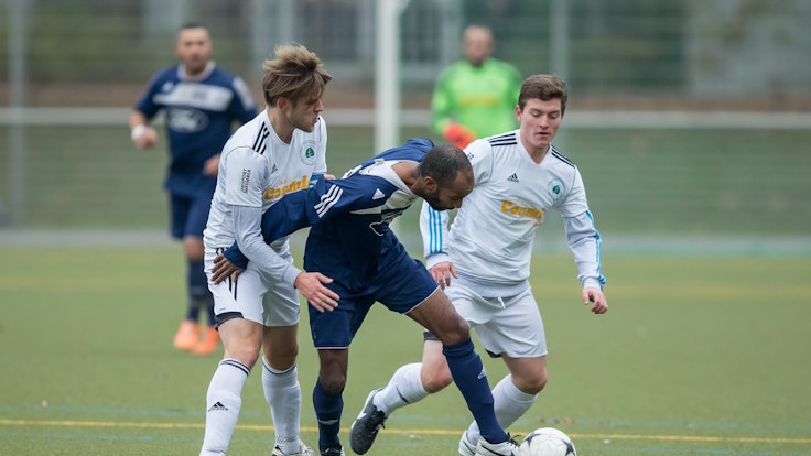Drei Fußballer kämpfen bei einem Amateurspiel um den Ball.