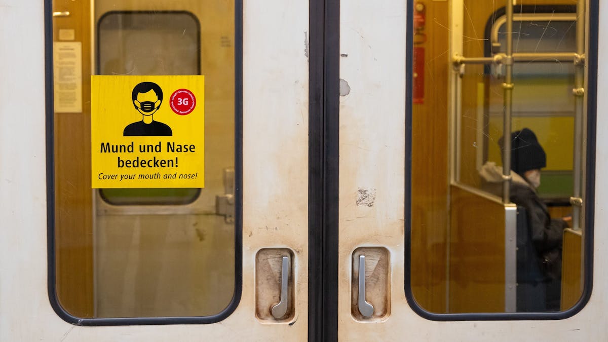 Ein Aufkleber mit der Aufschrift „Mund und Nase bedecken!“ ist an einer U-Bahn angebracht.