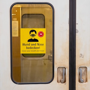 Ein Aufkleber mit der Aufschrift „Mund und Nase bedecken!“ ist an einer U-Bahn angebracht.