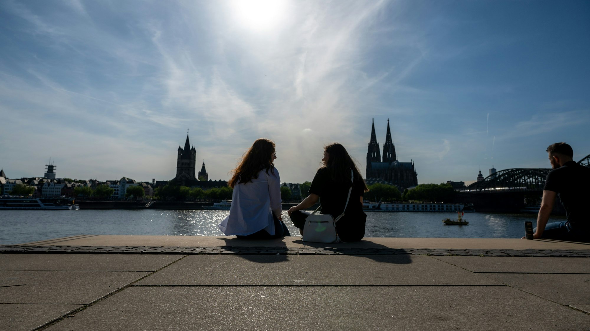 Zwei Frauen unterhalten sich am Rheinboulevard mit Blick zum Kölner Dom bei Sonnenschein.