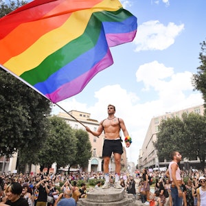 Menschen nehmen an der Pride-Parade in Bologna teil und ein Mann schwenkt eine große Regenbogenfahne.