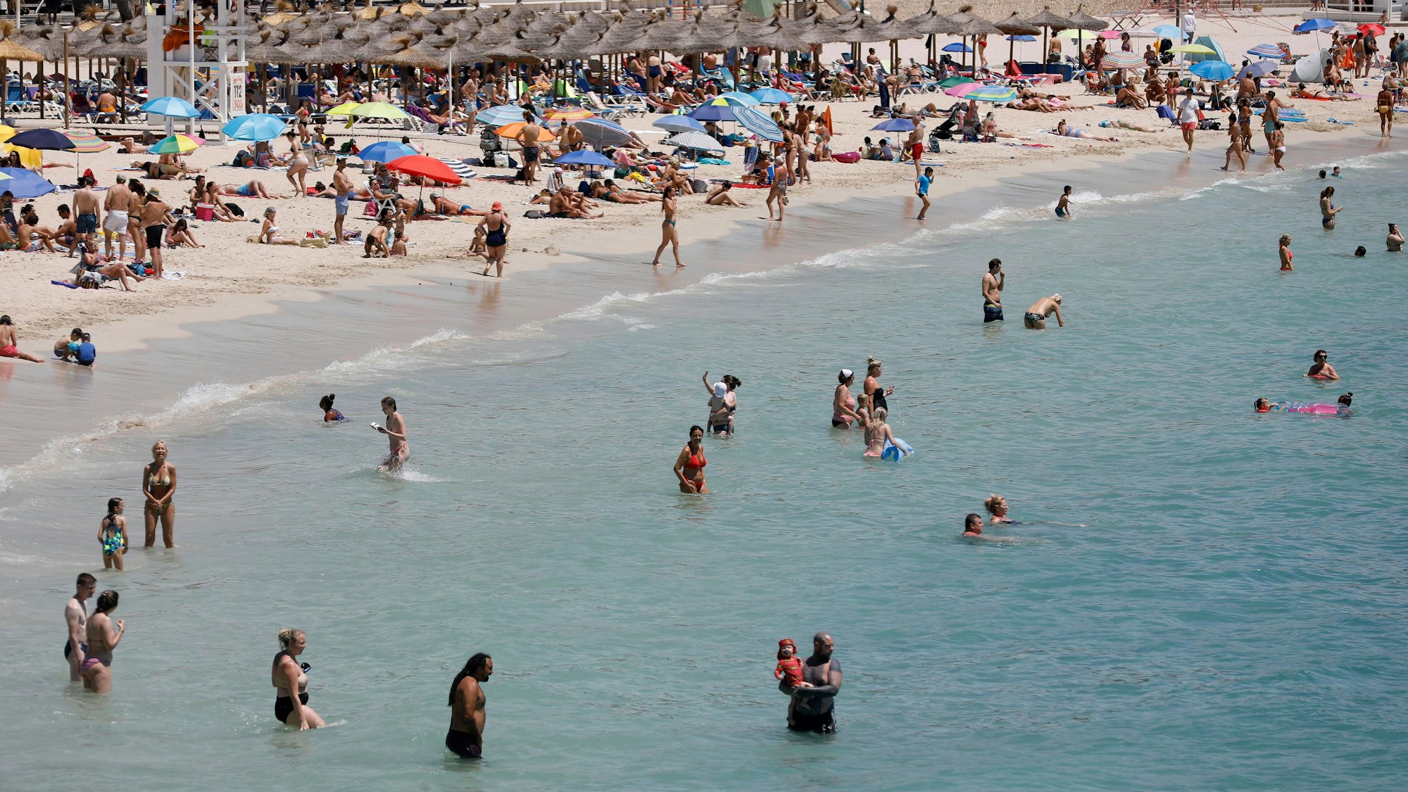 Menschen schwimmen und sonnen sich am Strand von Palmanova auf Mallorca. 