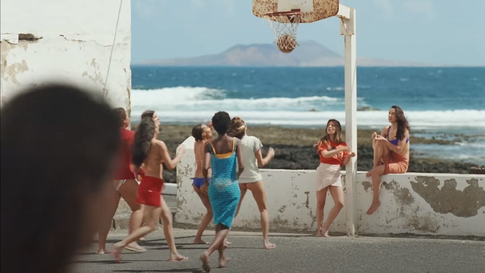 Screenshot aus dem Musikvideo „Provenza“ der kolumbianischen Sängerin Karol G. Mehrere Frauen spielen an der Promenade vor dem Meer Basketball.