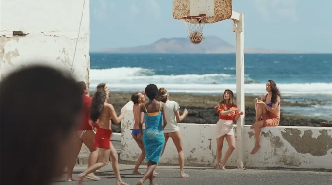 Screenshot aus dem Musikvideo „Provenza“ der kolumbianischen Sängerin Karol G. Mehrere Frauen spielen an der Promenade vor dem Meer Basketball.