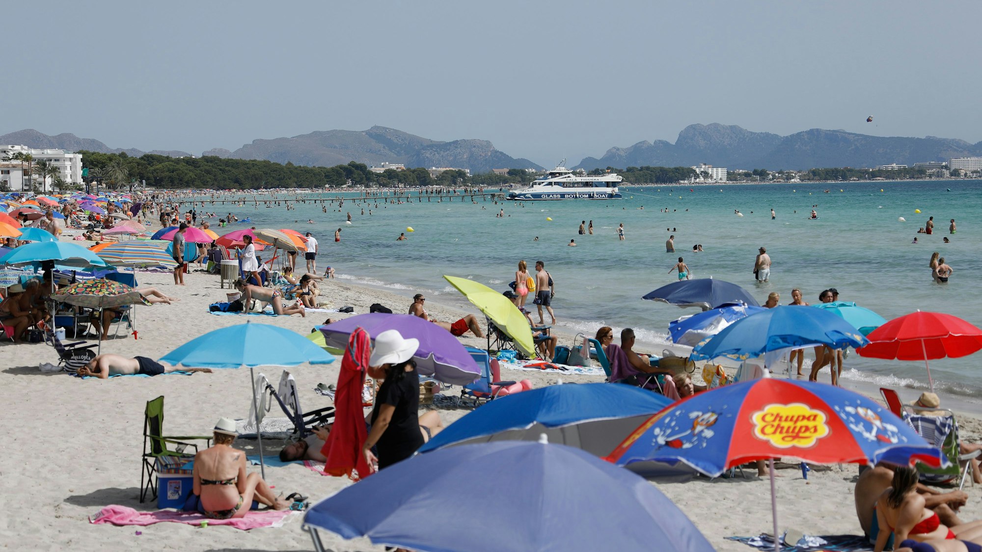 Unter bunten Sonnenschirmen genießen viele Menschen Sonne, Sand und Meer am Strand von Playa de Muro im Norden von Mallorca.