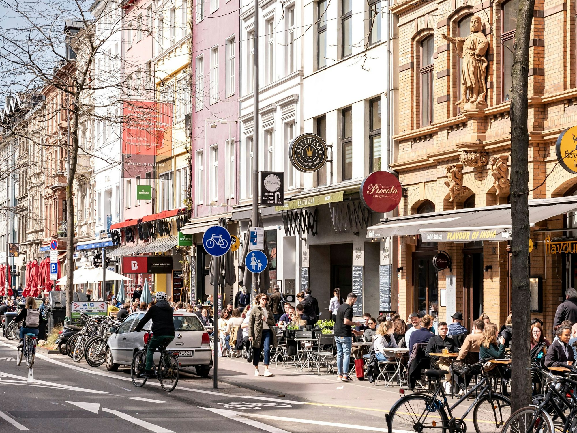 Menschen sitzen in Cafés am Straßenrand in Köln.