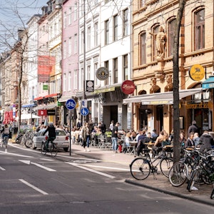Menschen sitzen in Cafés am Straßenrand in Köln.