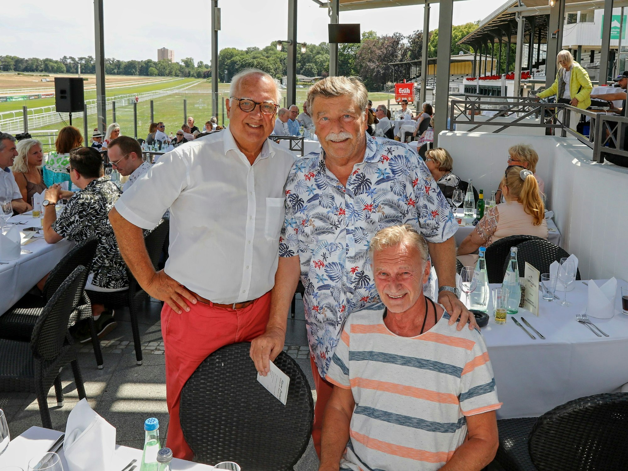 Drei Männer stehen in einem Restaurant und grinsen gemeinsam in die Kamera.
