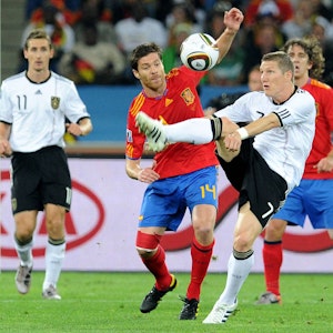 Deutschlands Bastian Schweinsteiger schlägt vor den Augen seines spanischen Gegenspielers Xabi Alonso den Ball weg. Im Hintergrund sind Miroslav Klose und Carles Puyol zu sehen.