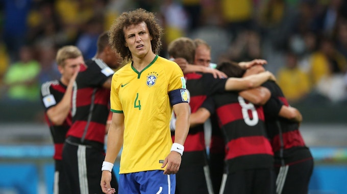 Brasiliens David Luiz schaut geknickt, im Hintergrund jubeln die deutschen Spieler.