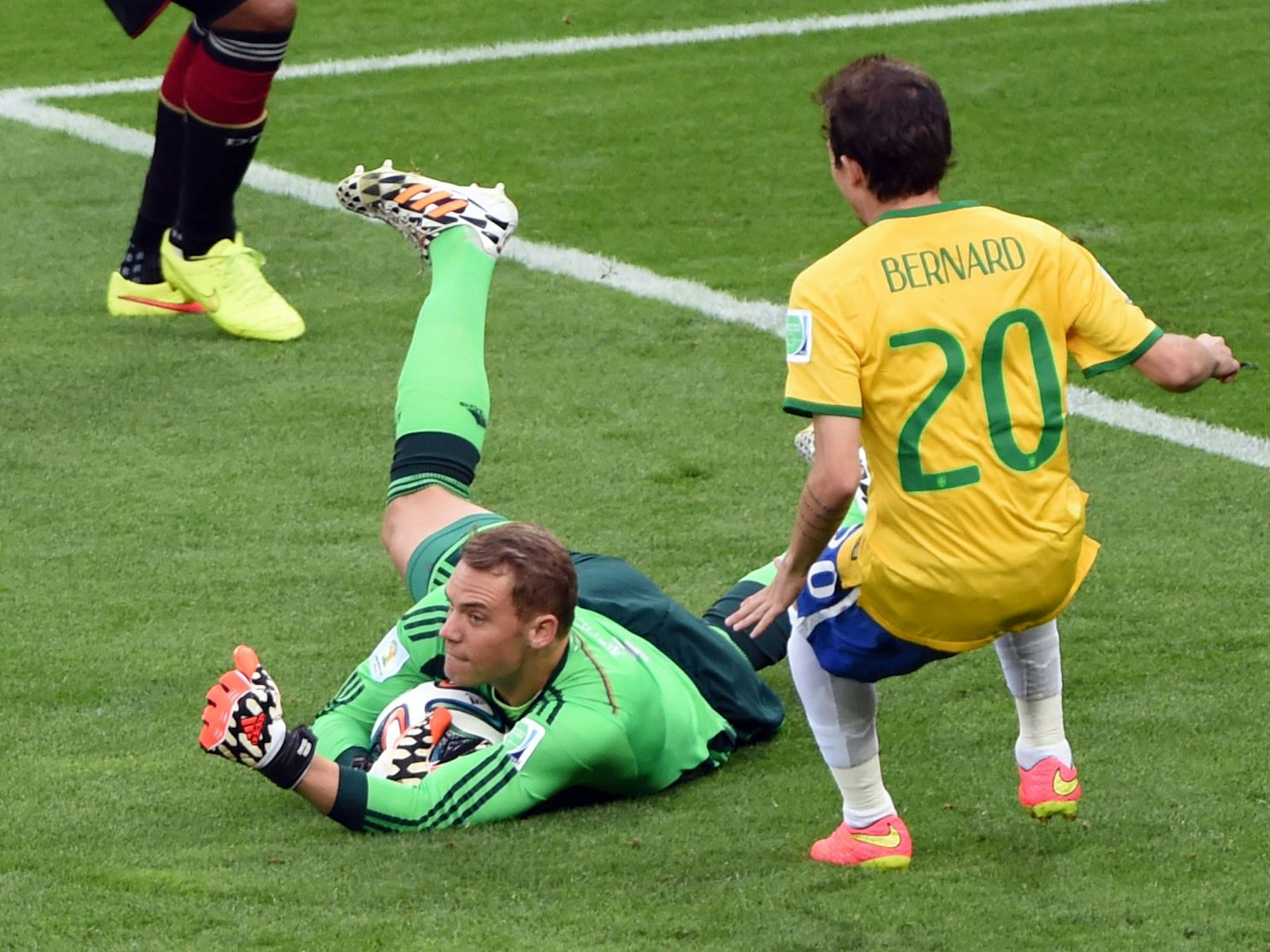 Torwart Manuel Neuer konnte erfolgreichen den Ball abfangen und liegt samt Ball auf dem Boden. Neben ihm steht Brasiliens Bernard.