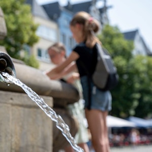 Eine Kölnerin kühlt sich an einem Brunnen in der Altstadt ab.