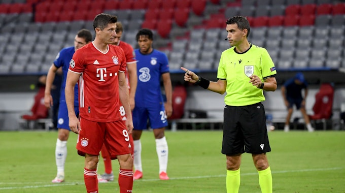 Bayern Münchens Robert Lewandowski steht neben Schiedsrichter Ovidiu Hațegan aus Rumänien vor seinem Elfmeter.