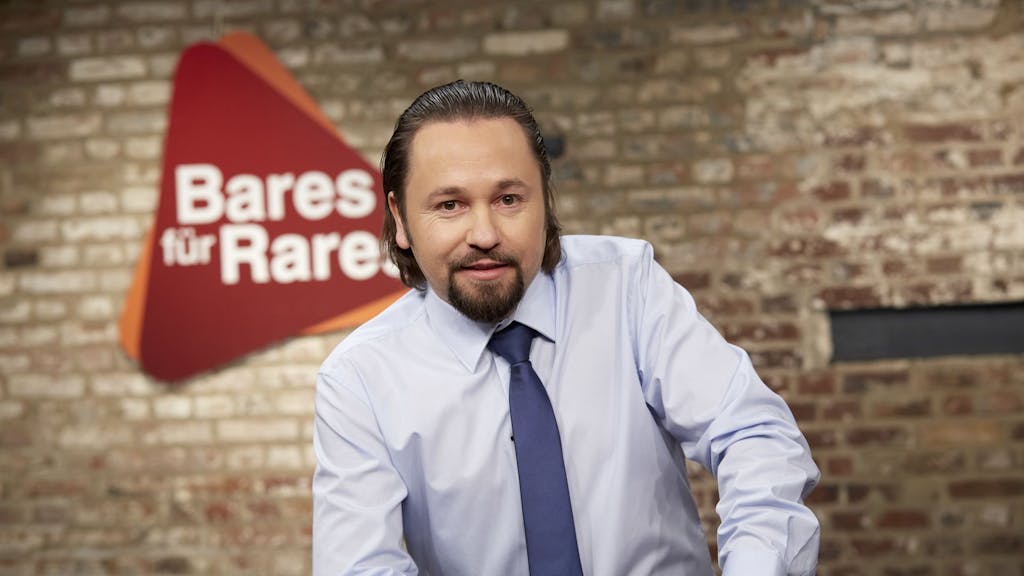„Bares für Rares“-Händler Wolfgang Pauritsch posiert in der Kulisse der Show für ein Pressefoto.