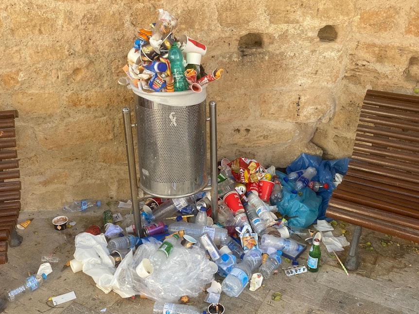 Den Gemeinden ist das Müll-Problem auf Mallorca bekannt. Unser Foto zeigt einen überquellenden Mülleimer und Abfall auf dem Boden, aufgenommen in Port d'Alcúdia auf Mallorca am 14. Juli 2022.