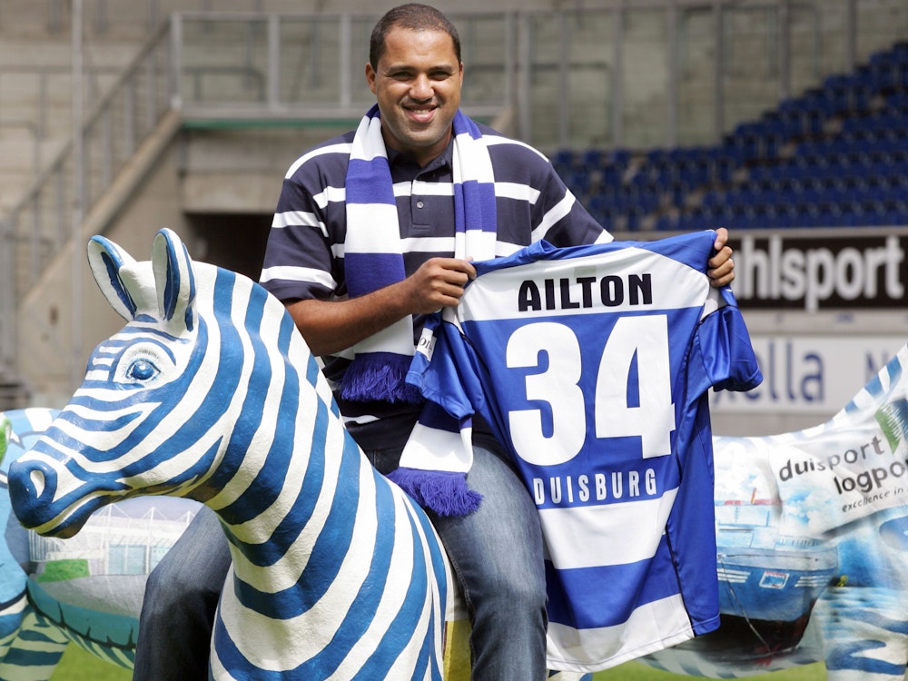Der brasilianische Fußball-Profi Ailton posiert in Duisburg mit seinem neuen Trikot auf dem Zebra-Maskottchen des Bundesligisten MSV Duisburg.