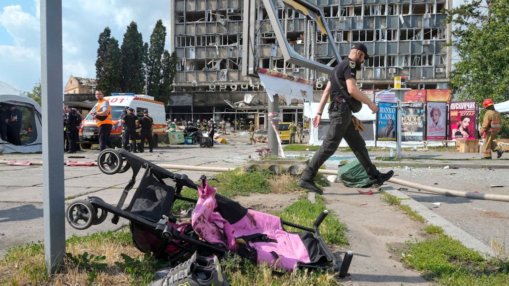 Ein mit Blut verschmierter Kinderwagen, im Hintergrund ein durch russische Bomben zerstörtes Haus. Hätte der ukrainische Präsident das wirklich verhindern können, fragt unsere Kollegin.