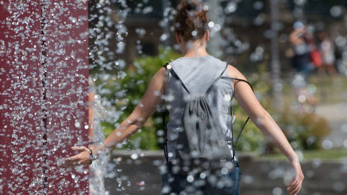 Eine Frau kühlt sich an einem Springbrunnen ab.