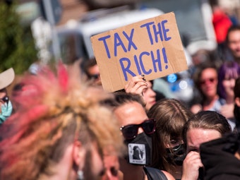 Teilnehmer einer Demonstrantion des Bündnisses „Wer hat, der gibt“ halten ein Schild mit der Aufschrift „Tax The Rich!“.