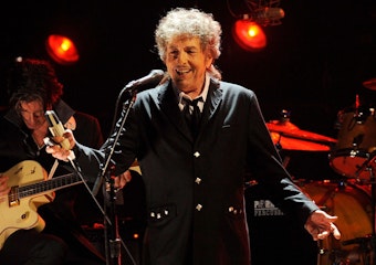 Bob Dylan steht mit Mikrofon auf der Bühne und singt einen Song.