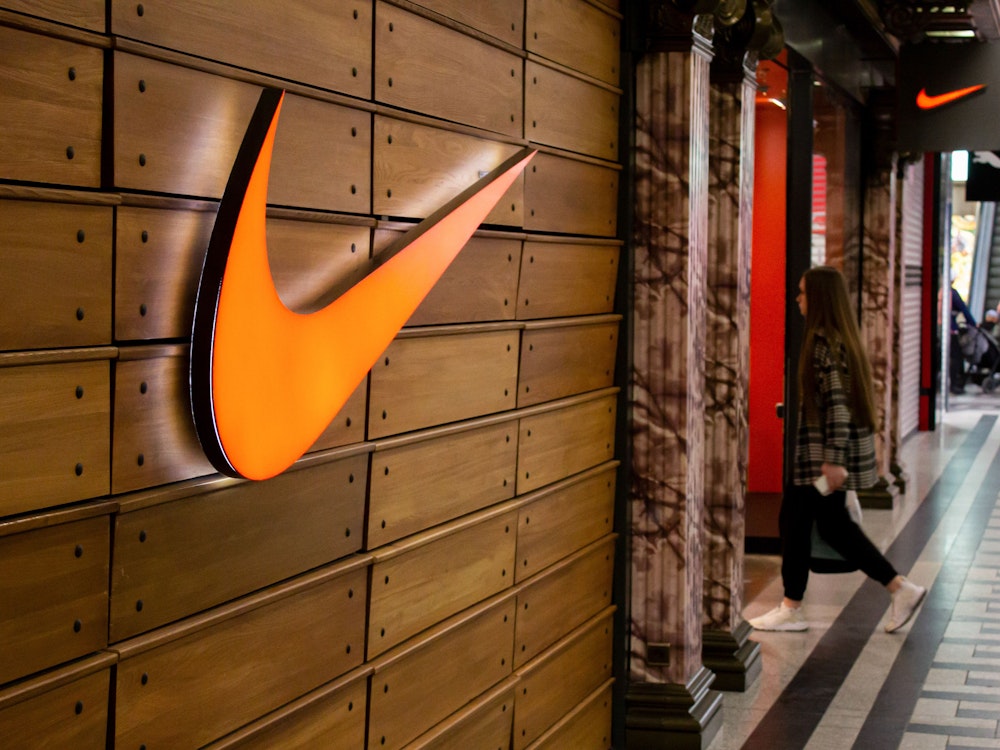 Eine Frau betritt eine Nike-Boutique in einem Einkaufszentrum. Das große Logo des Sportartikelherstellers leuchtet orange.