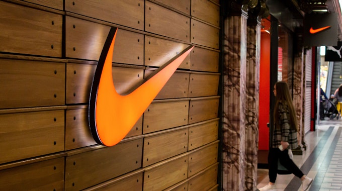 Eine Frau betritt eine Nike-Boutique in einem Einkaufszentrum. Das große Logo des Sportartikelherstellers leuchtet orange.