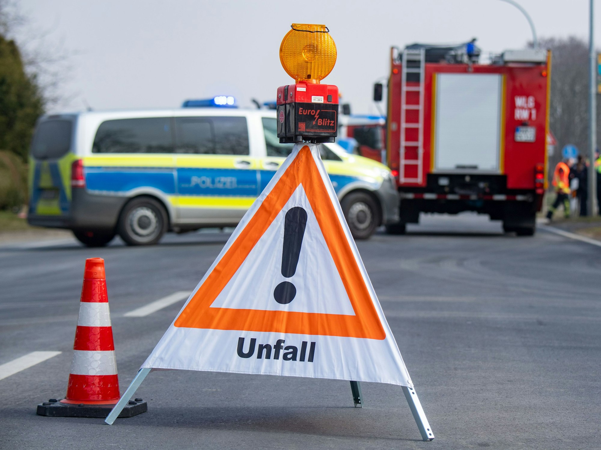 Ein Schild mit dem Hinweis „Unfall“ steht auf der Straße und hinten stehen Polizei- und Feuerwehrfahrzeuge.