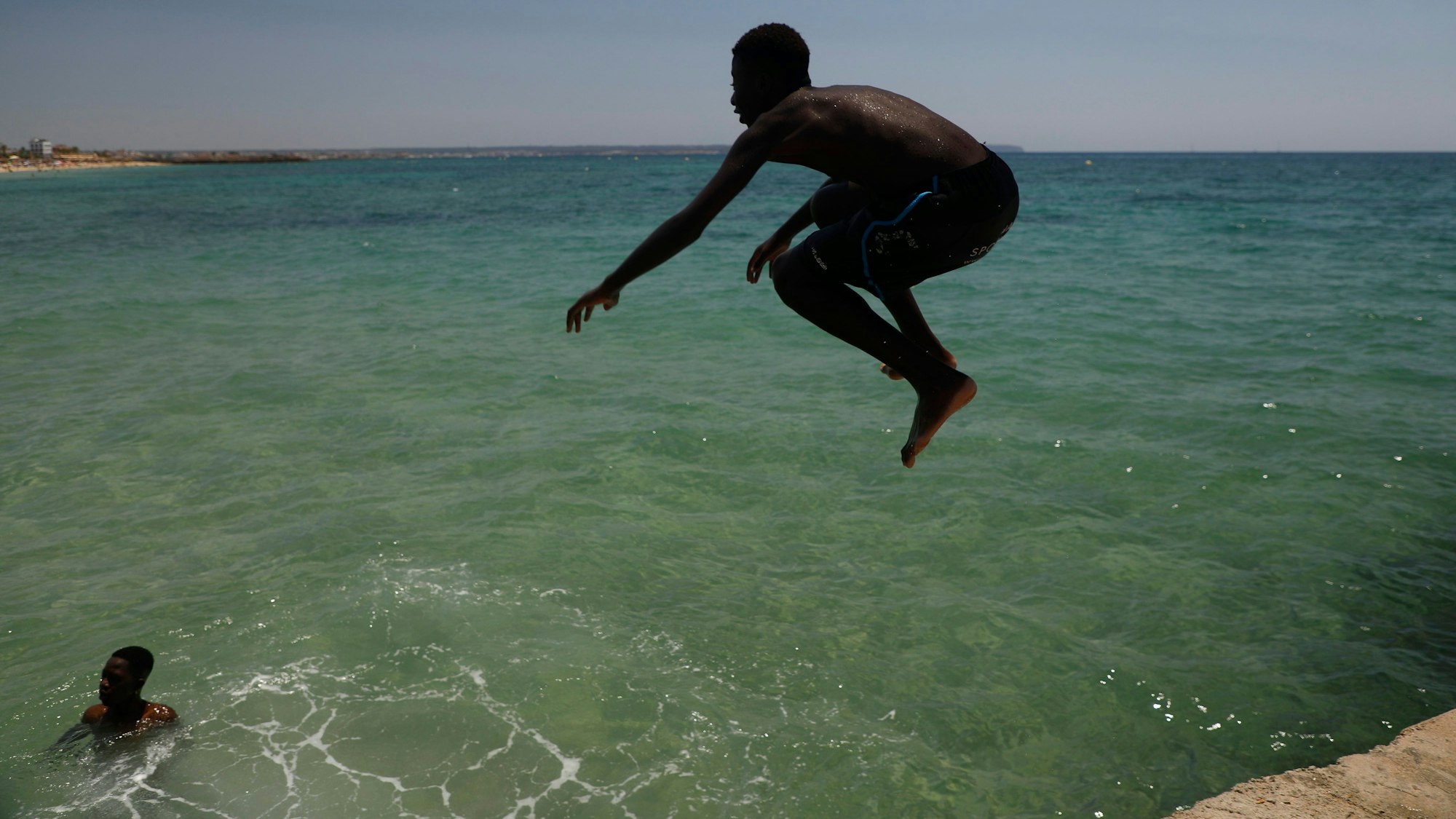Ein Junge springt während der Hitzewelle am Strand Can Pere Antoni ins Meer.