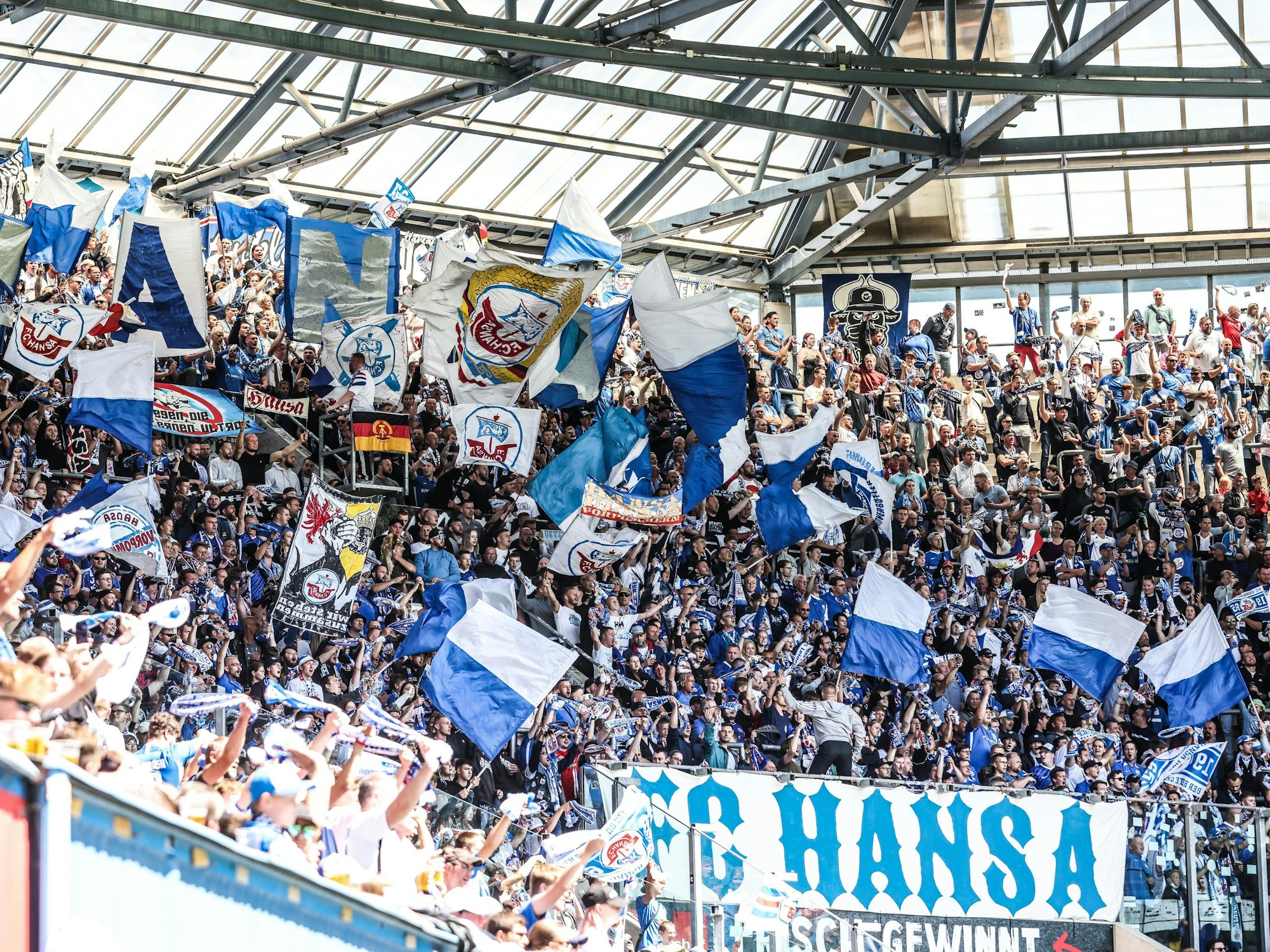 Die Fans des FC Hansa Rostock schwenken Fahnen in der Kurve des Ostseestadions.