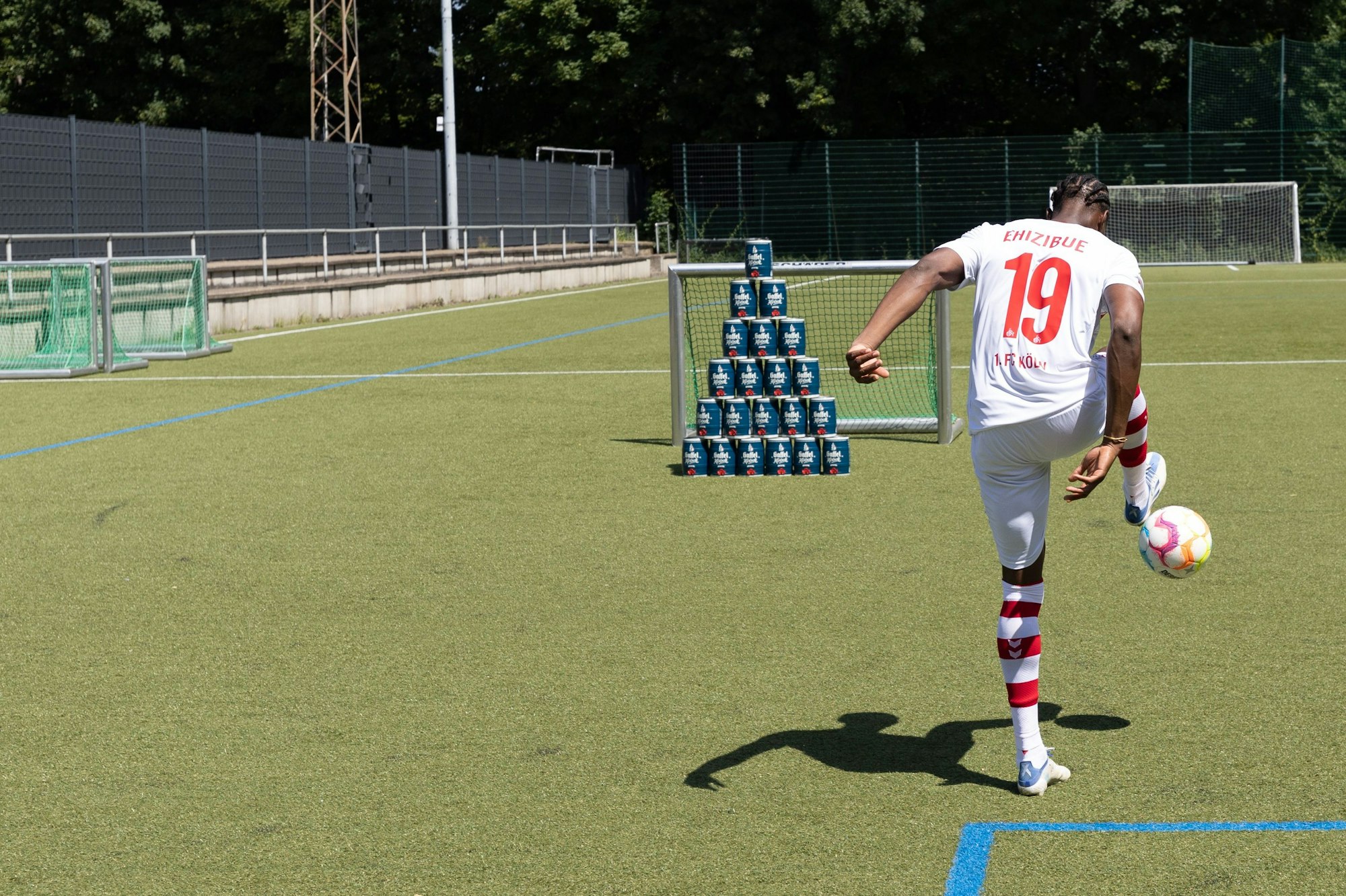 Kingsley Ehizibue zielt auf eine beim Media-Day des 1. FC Köln aufgebaute Dosen-Pyramide aus Kölsch-Fässchen.