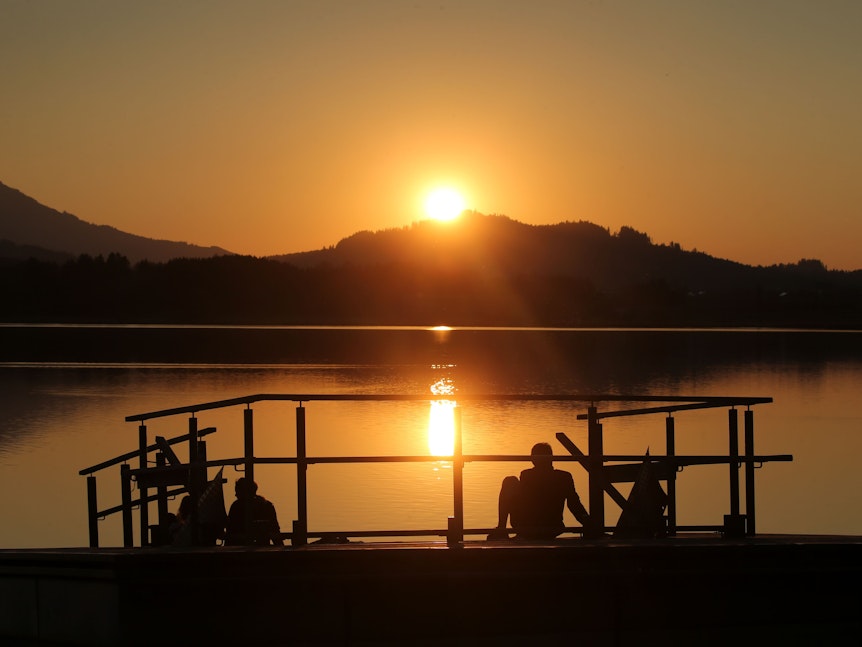 Menschen genießen am Ufer des Hopfensees den Sonnenuntergang.