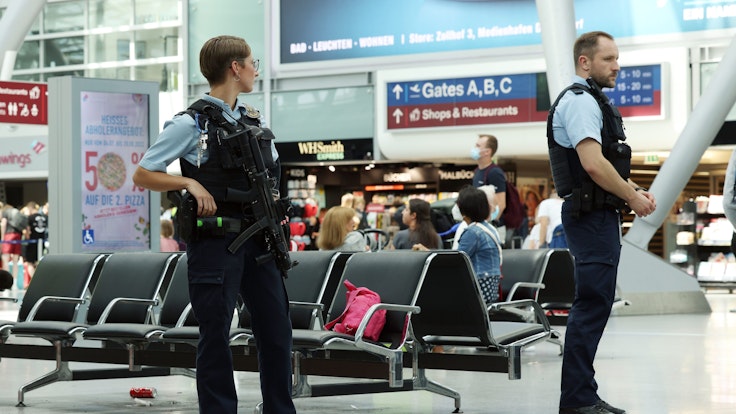 Eine Bundespolizistin und ein Bundespolizist stehen im Flughafen Düsseldorf.