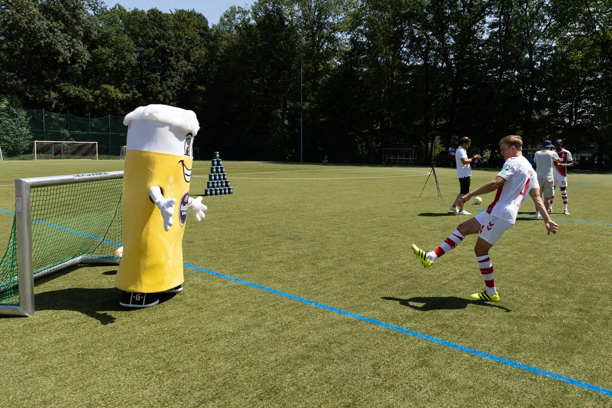 Timo Hübers schießt beim Media-Day des 1. FC Köln an einem als Kölschglas kostümierten Torwart vorbei auf ein kleines Tor.