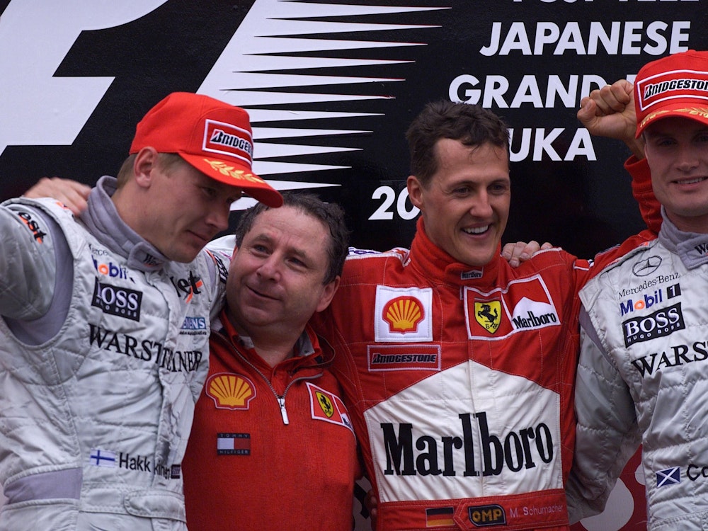 Mika Hakkinen (links), Jean Todt (2.v.l.), Michael Schumacher (2.v.r.) und David Coulthard (rechts) auf dem Podium Arm in Arm.