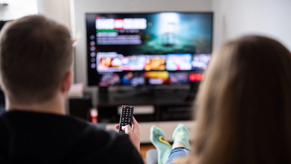 Zuschauer sitzen vor einem Fernseher und schauen sich das Streaming-Angebot ihrer Abonnements an.