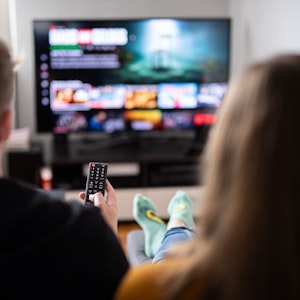 Zuschauer sitzen vor einem Fernseher und schauen sich das Streaming-Angebot ihrer Abonnements an.