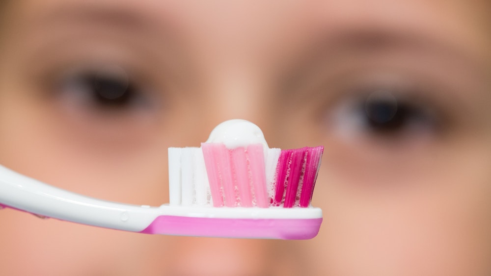 Eine Achtjährige schaut ihre Zahnbürste mit Zahnpasta an.