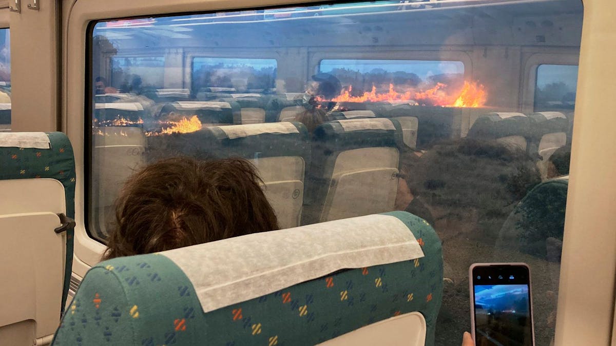 Fahrgäste fotografieren während einer Zugfahrt in Spanien einen Flächenbrand. Der Zug hielt unterwartet in einer Region an, in der sich die Flammen ausbreiteten.