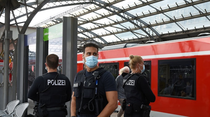 Eine Bundespolizistin und zwei Kollegen stehen auf einem Gleis im Kölner Hauptbahnhof.