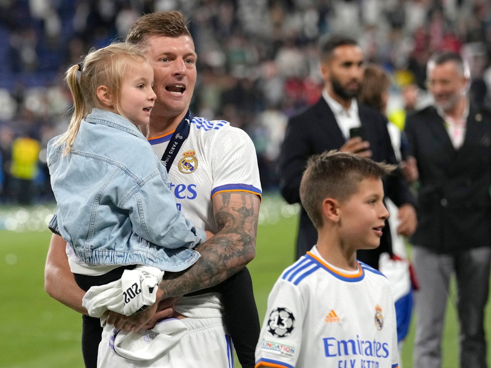 Toni Kroos steht auf dem Platz und hält seine Tochter auf dem Arm, daneben sein Sohn.