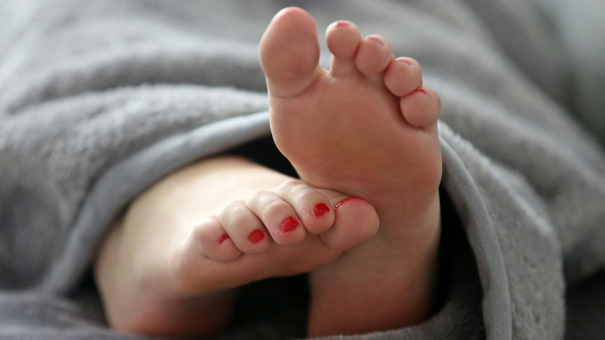 Eine Frau schläft in einemBett und streckt die Füße unter der Decke hervor.